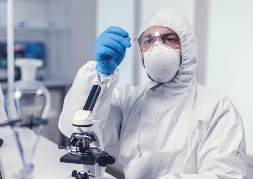 At Rushabh Pathology Laboratory, a man in a lab coat and mask examines a microscope, showcasing dedication to pathology.
